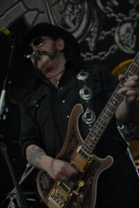 Close-up portrait of Lemmy Kilmister of Motörhead wearing his signature black cavalry hat, iron cross necklace, and denim vest