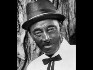 Mississippi Fred McDowell performing acoustic bottleneck slide guitar with a thumb-picking technique.