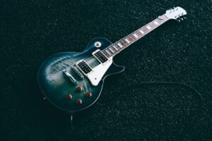 A blue-green flamed maple top Les Paul style electric guitar lying flat on a dark textured background with an attached guitar cable.